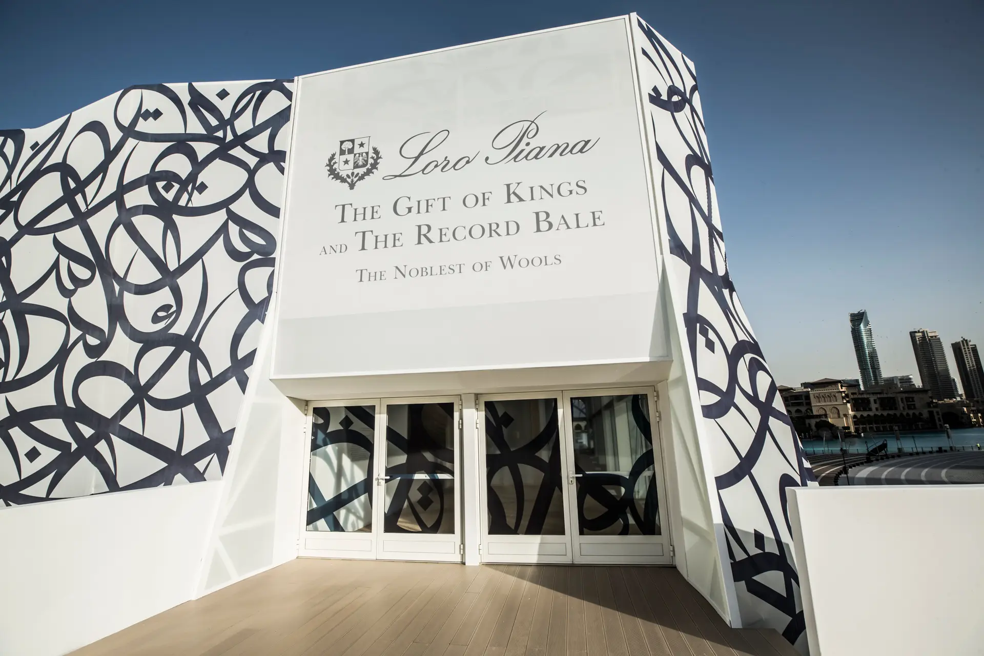 The exterior of a temporary exhibition pavilion with signage reading Loro Piana – The Gift of Kings and The Record Bale: The Noblest of Wools, set against a city skyline.